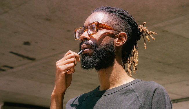 A man wearing brown glasses is smoking a wax pen.
